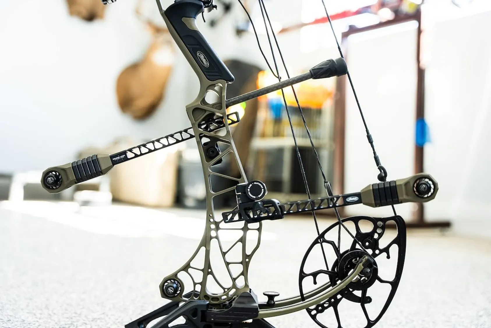 Modern compound bow with skeletal riser design and cam system displayed on white surface in indoor setting