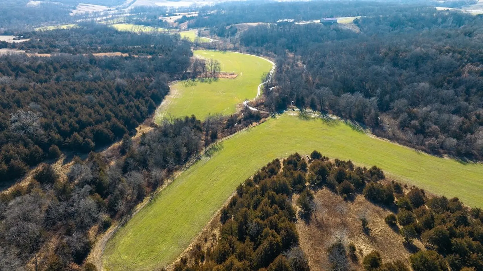 Aerial view of rolling green pastures separated by wooded valleys and hills in rural landscape.